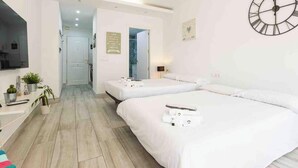 A hotel room with two beds, a TV, a plant, and a clock on the wall. - 'El Ciaboga' Apartment with Wi-Fi and Air Conditioning (Torremolinos)