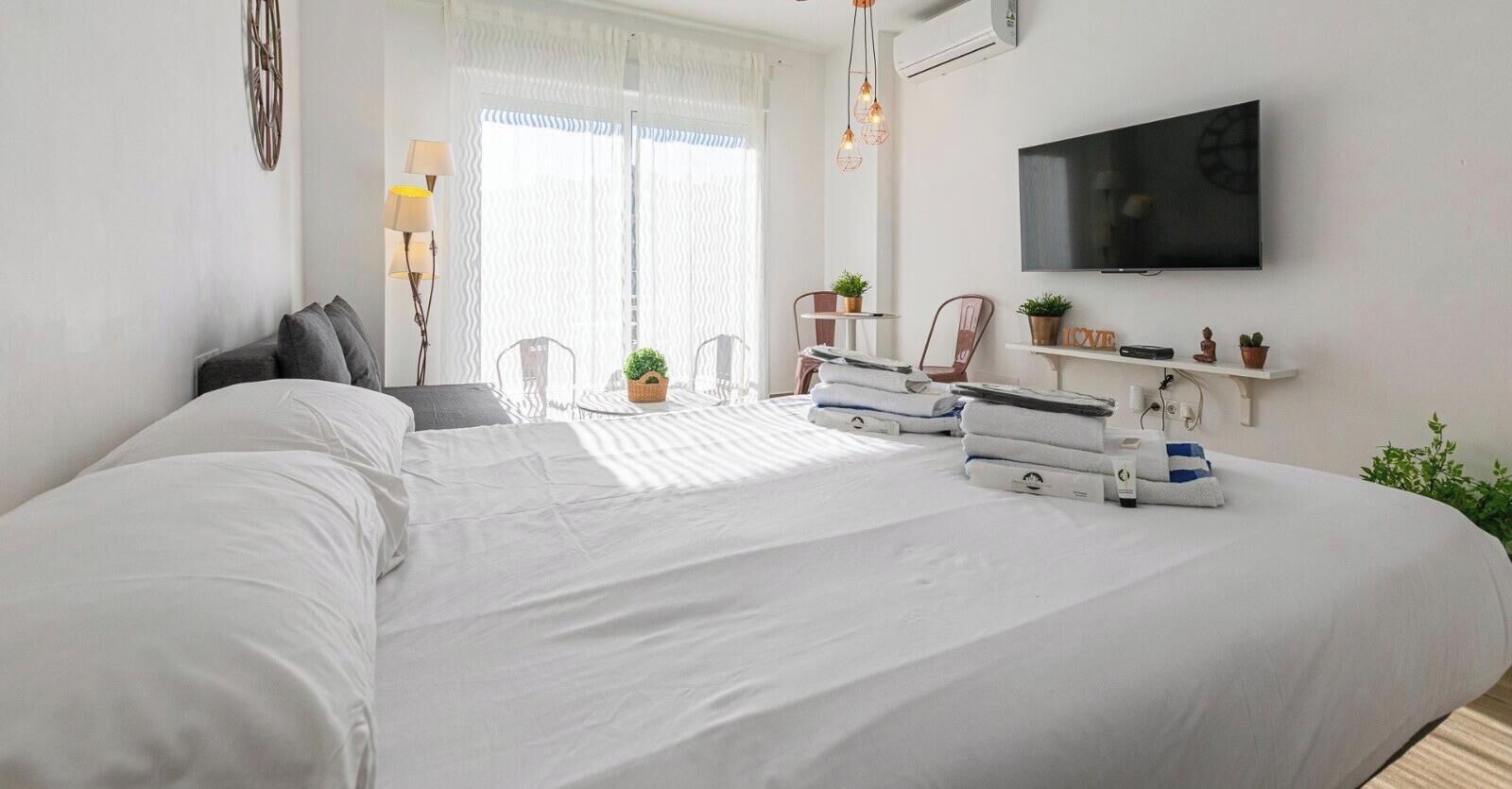 Ein Hotelzimmer mit einem großen Bett, einem flachbildfernseher an der Wand, einem kleinen Tisch mit Stühlen und einem Fenster mit Vorhängen.