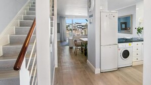 Una cocina moderna con lavadora integrada, una zona de comedor con mesa y sillas, y una escalera que conduce a otro nivel.