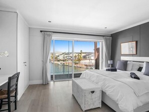 Ein modernes Schlafzimmer mit einem großen Bett, einem weißen Korboottman und Blick auf eine Wohngegend durch eine Schiebetür.