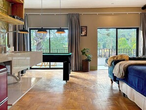 Une pièce avec une table de billard, un lit, une plante en pot et une vue sur l’extérieur.