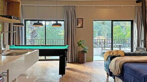 Una habitación con mesa de billar, cama, ventana grande y una planta.