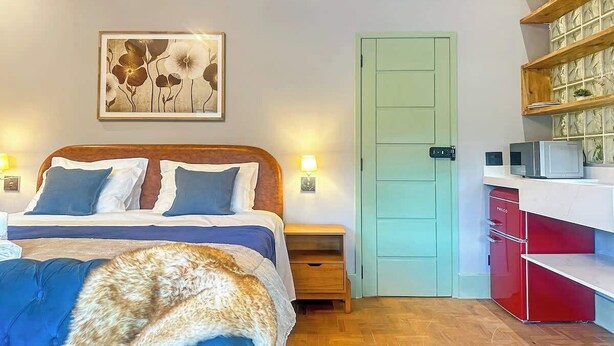 Un dormitorio con cama, mesitas de noche, una puerta y una pequeña cocina.