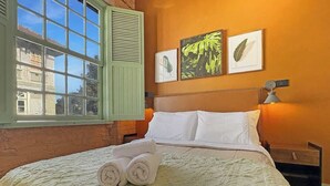 Quarto de hotel com cama, janela com persianas, mesa de cabeceira e decoração nas paredes.