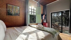 Ein Schlafzimmer mit Bett, einem Fenster mit Rollläden, einem Gemälde an der Wand und Blick ins Freie.