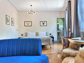 Quarto com cama, sofá azul, mesa de jantar e lustre.