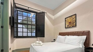 Una camera d'hotel con un letto, una finestra con persiane, un quadro appeso al muro e un pavimento in legno.