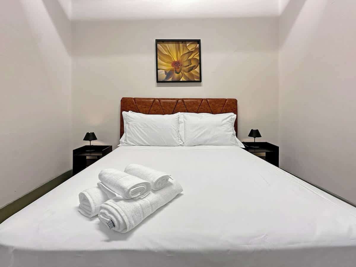 A hotel room with a neatly made bed, two bedside tables with lamps, and a framed artwork on the wall.