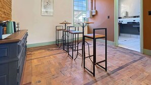 A room with a kitchen area, a dining table with chairs, and a wooden floor.