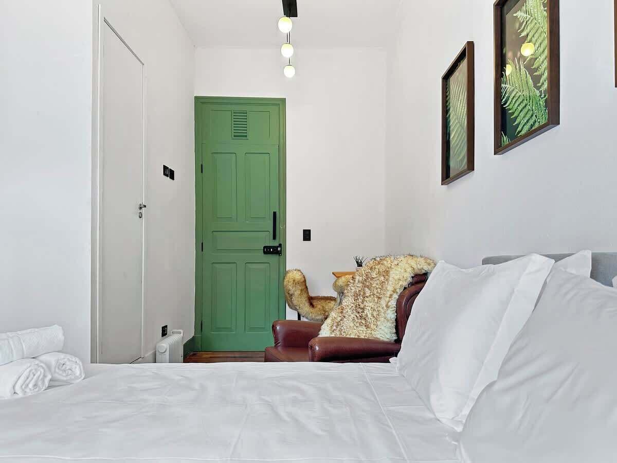 Ein Schlafzimmer mit einem Bett, einer grünen Tür, einem Stuhl und einer Wandleuchte.