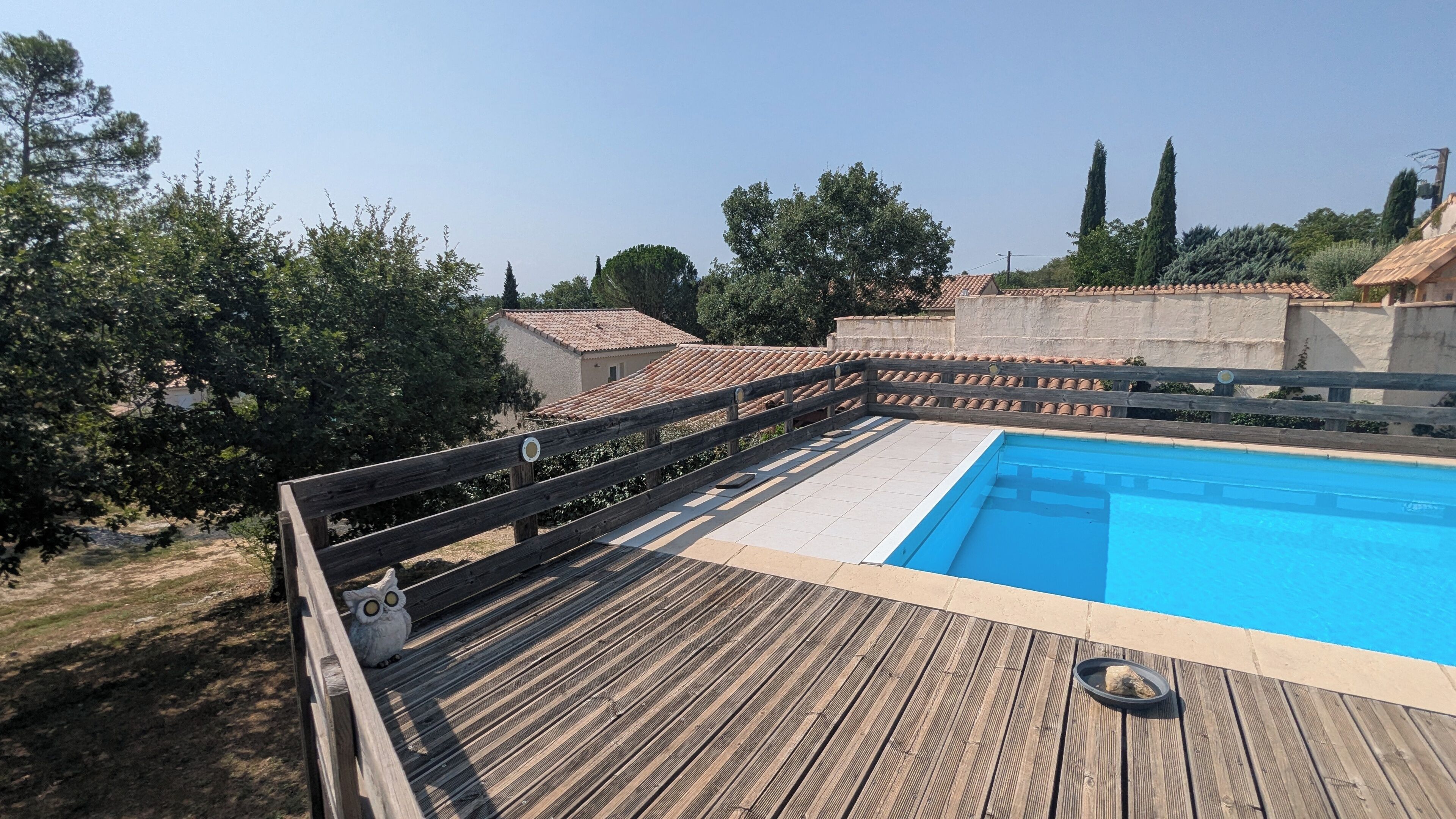 Une terrasse en bois avec une piscine, entourée d’arbres et d’immeubles aux toits recouverts de tuiles.