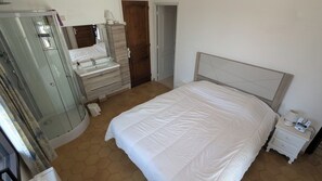 Ein Schlafzimmer mit Bett, Schminktisch, Spiegel, Nachttisch und Dusche.