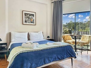 A hotel room with a bed, a view of the outdoors, and a balcony with chairs. - Villa_Aberdeen_02 · Pousada Villa Aberdeen, Quarto 02 (Campos do Jordão)