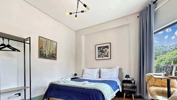 Una camera da letto con un letto, un comodino, una sedia, un appendiabiti e una finestra con vista.