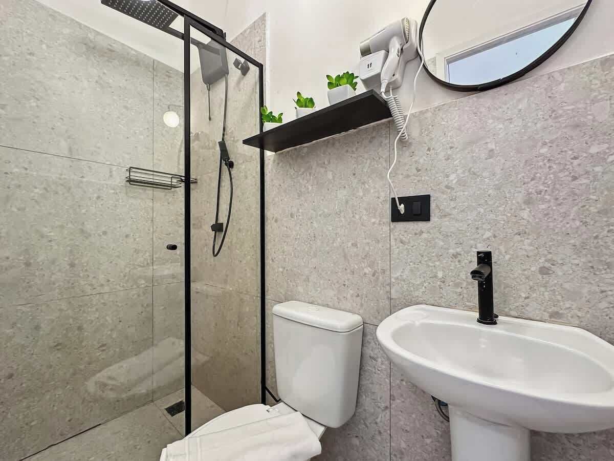 Een moderne badkamer met een douchecabine van glas, een toilet, een wastafel en een haardroger op een plank.