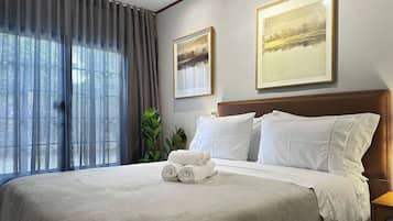 A hotel room with a large bed, two framed pictures on the wall, a window with curtains, and a bedside table.