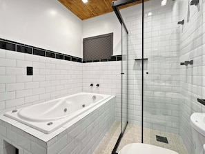 Un baño moderno con azulejos blancos tipo metro, ducha con mampara de vidrio y bañera blanca.