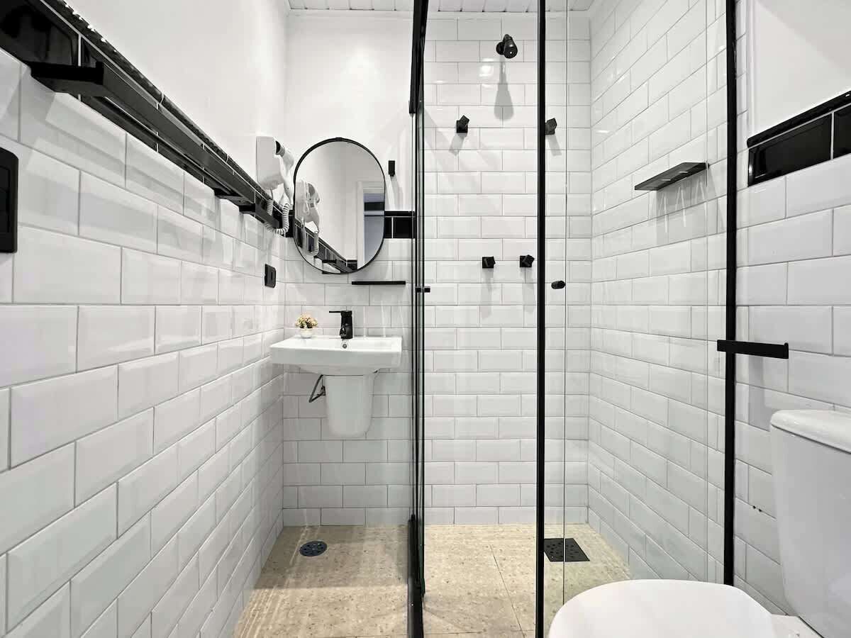 A modern bathroom with white subway tiles, a glass shower enclosure, a sink with a mirror, and a toilet.