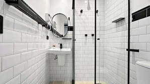 Un baño moderno con azulejos blancos tipo metro, una cabina de ducha de vidrio, un lavamanos con espejo y un inodoro.
