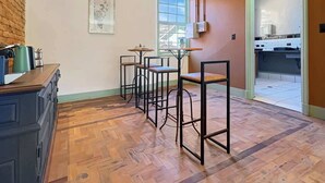 Una cocina con piso de madera en patrón de espiga, una barra con taburetes, un refrigerador y una ventana.