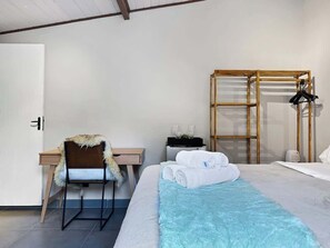 A hotel room with a bed, a desk, a chair, a wardrobe, and a bedside table.