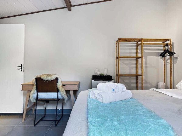 A hotel room with a bed, a desk, a chair, a wardrobe, and a bedside table.