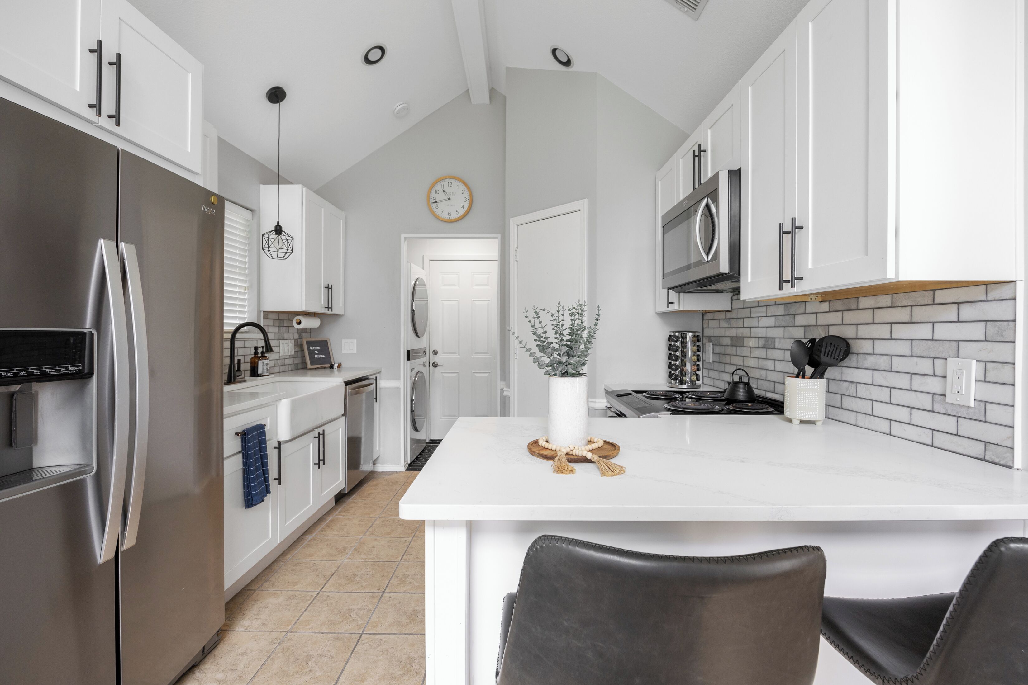 Una cocina moderna con muebles blancos, un refrigerador de acero inoxidable, una isla central y un microondas.