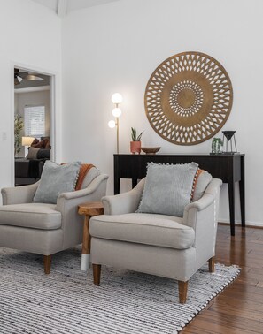 A living room with two armchairs, a round decorative wall piece, a small wooden side table, and a floor lamp with three lights. - Steps from Main street, Updated Family-Friendly Home with Fireplace and Garage! (Frisco)
