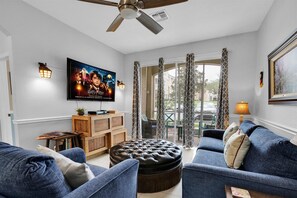 A living room with a television, sofas, a coffee table, and a ceiling fan. - Last Minute Disney Getaway! Themed Bedrooms & Private Balcony. Book Now! #98463 (Orlando)