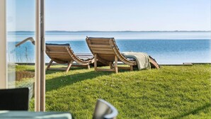 Two wooden lounge chairs on a grassy lawn with a view of a calm body of water. - 5 Star Holiday Home in Svendborg (Svendborg)