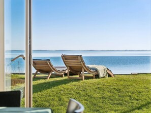 Two wooden lounge chairs on a grassy lawn with a view of a calm body of water. - 5 Star Holiday Home in Svendborg (Svendborg)