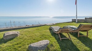 A grassy area with two wooden lounge chairs facing a body of water, a flagpole, and a clear sky. - 5 Star Holiday Home in Svendborg (Svendborg)