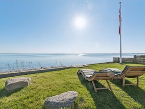 A grassy area with two wooden lounge chairs facing a body of water, a flagpole, and a clear sky. - 5 Star Holiday Home in Svendborg (Svendborg)