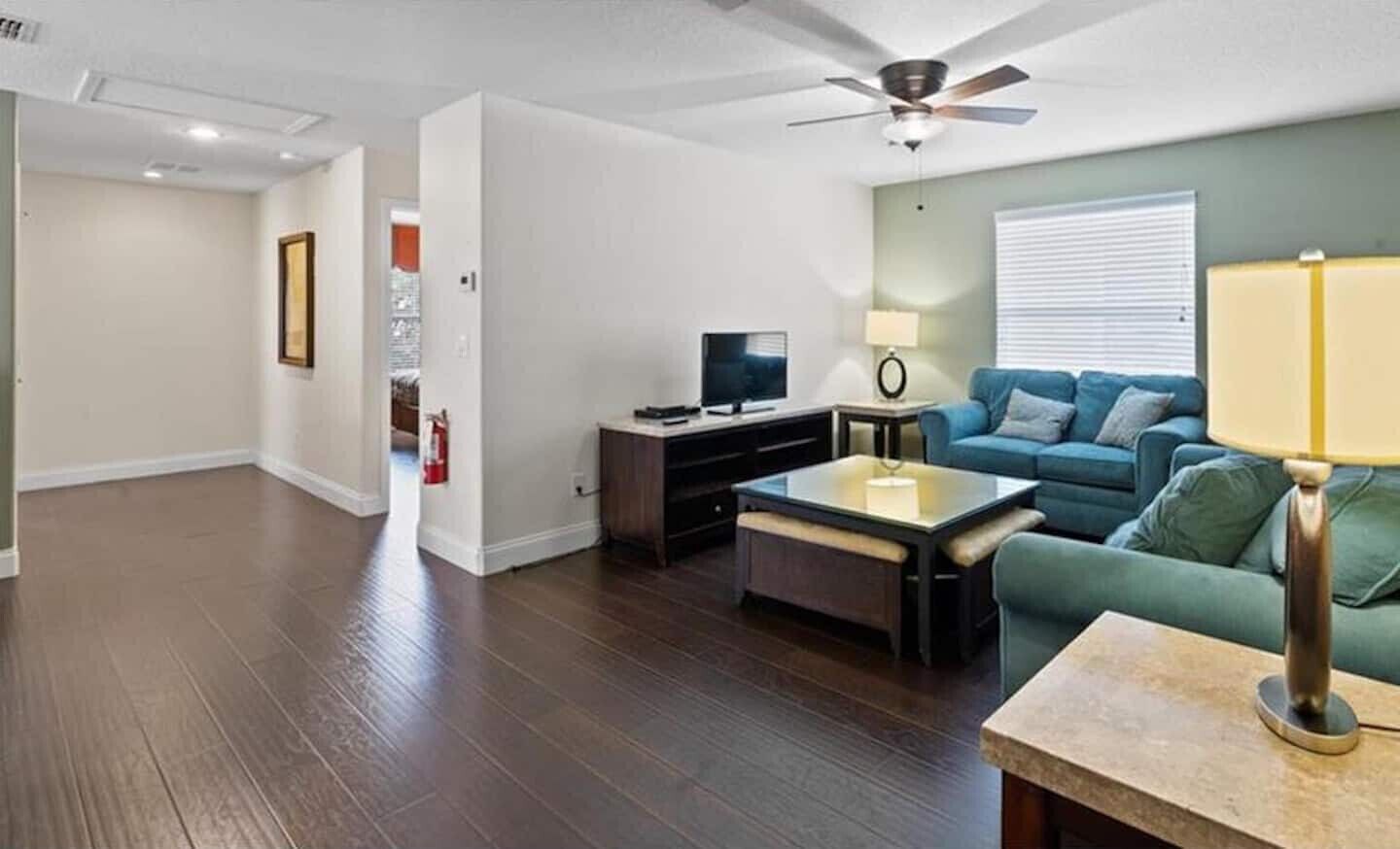 Un salon moderne avec un téléviseur à écran plat, un canapé bleu, une table basse et un ventilateur de plafond.