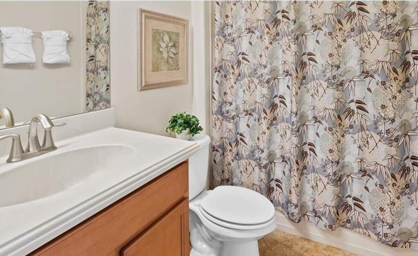 Ein Badezimmer mit einem weißen Waschbecken, einer Toilette und einer blumengemusterten Duschvorhang.