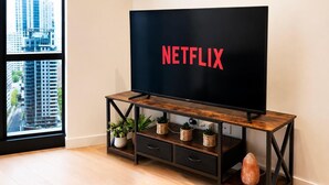 A modern living room with a large flat-screen TV on a wooden TV stand, a potted plant, and a decorative stone. - Sea & Skyline Views | Pool, Gym & Sauna (Southbank)