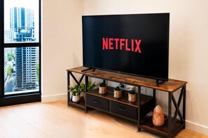 Ein modernes Wohnzimmer mit einem großen Flachbildfernseher auf einem hölzernen TV-Schrank, einer Topfpflanze und einem dekorativen Stein.