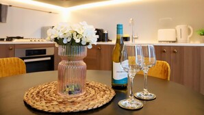 A modern kitchen with a dining table set for two, featuring a bottle of wine and two glasses. - Sea & Skyline Views | Pool, Gym & Sauna (Southbank)