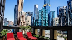 A modern rooftop terrace with red lounge chairs, a view of a city skyline, and a glass railing. - Sea & Skyline Views | Pool, Gym & Sauna (Southbank)