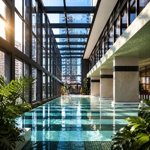 An indoor swimming pool with clear glass walls, surrounded by potted plants and a modern architectural design. - Sea & Skyline Views | Pool, Gym & Sauna (Southbank)