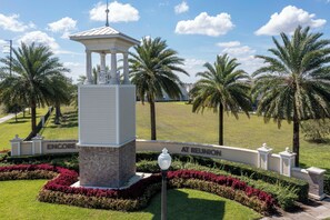 Un gazebo con tetto bianco e colonne, circondato da siepi curate e palme.