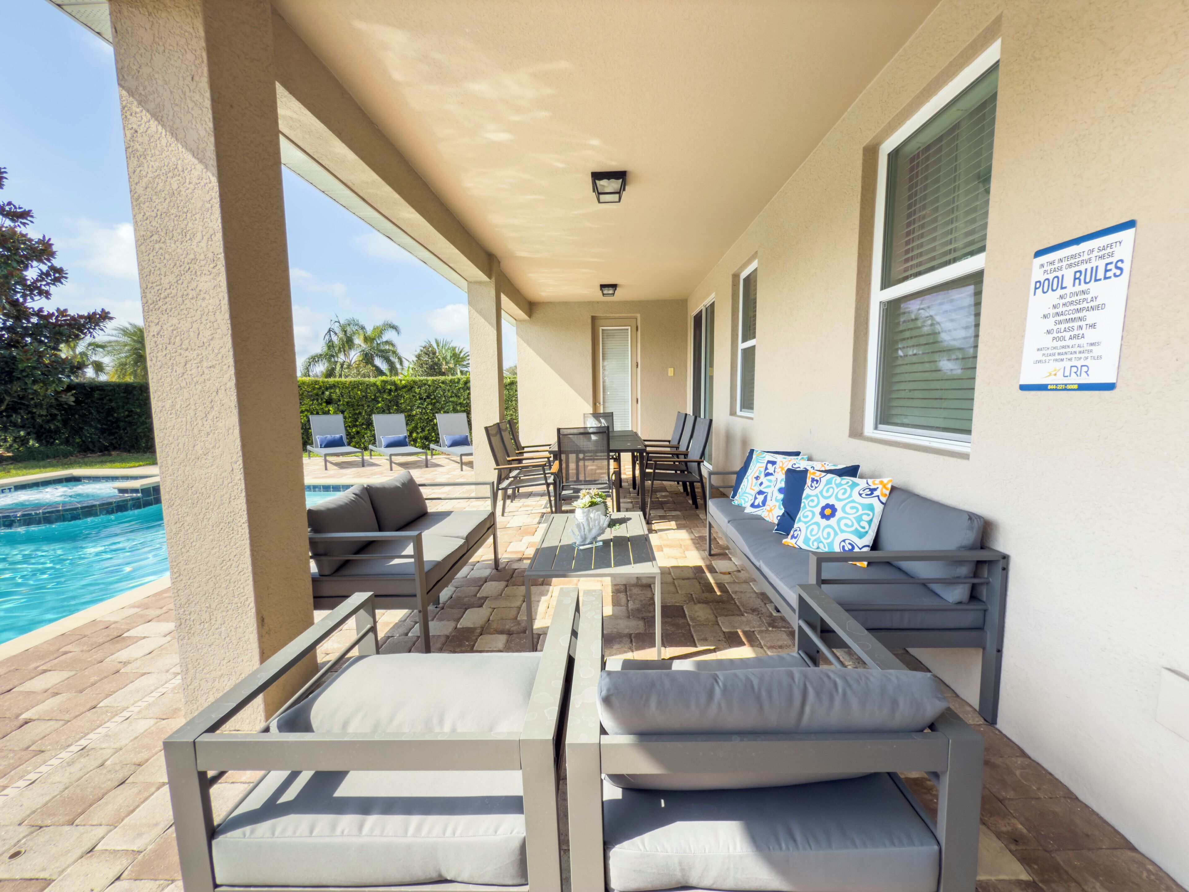 A covered outdoor seating area with poolside furniture, a table, and chairs.