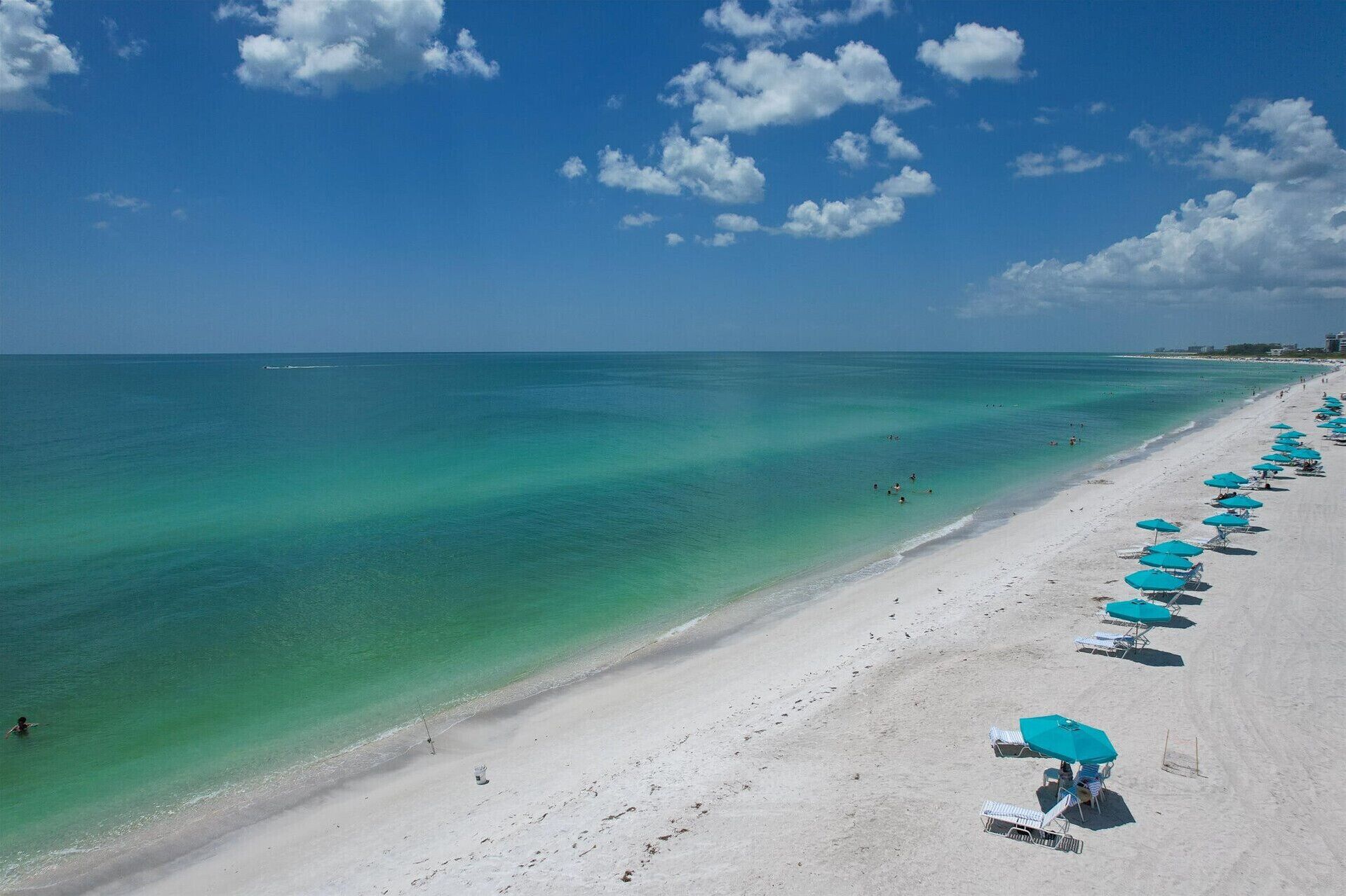 A beach with clear turquoise water, white sand, and a row of blue umbrellas.