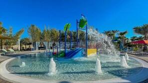 Un espace de jeux aquatiques avec des toboggans et des fontaines, entouré de palmiers et de chaises longues.