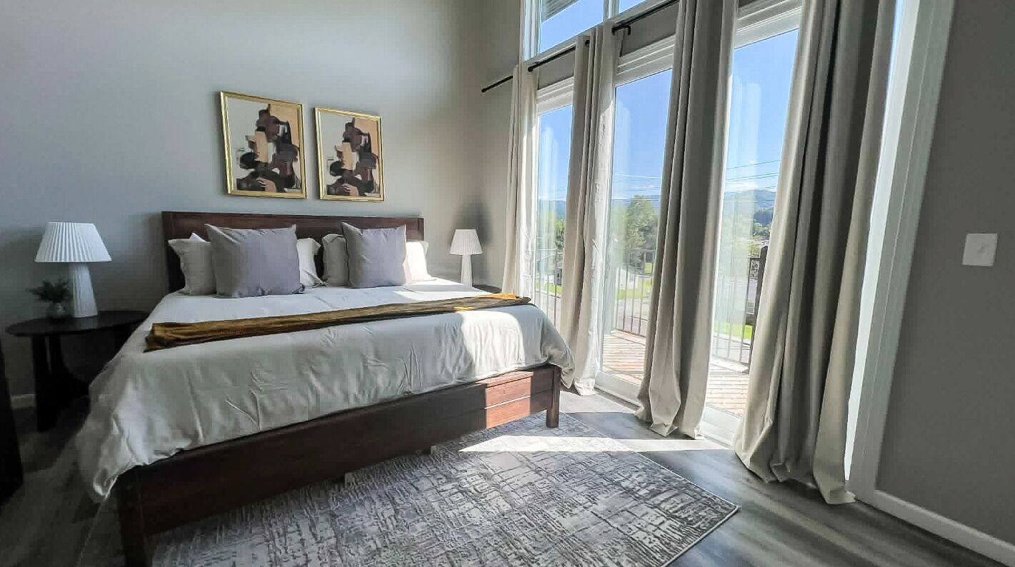 A bedroom with a large bed, two bedside lamps, a rug, and a view through a sliding glass door.