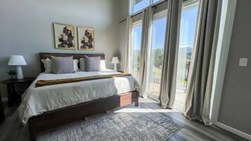A bedroom with a large bed, two bedside lamps, a rug, and a view through a sliding glass door.