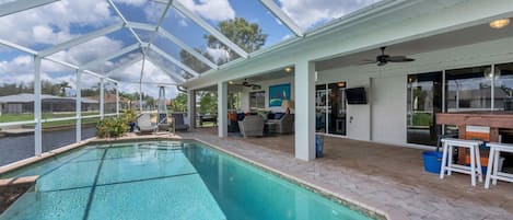 A covered outdoor swimming pool with a patio area, a ceiling fan, and a view of a body of water.