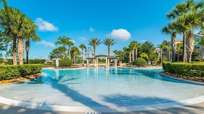 Une grande piscine extérieure entourée de palmiers et un pavillon abrité.