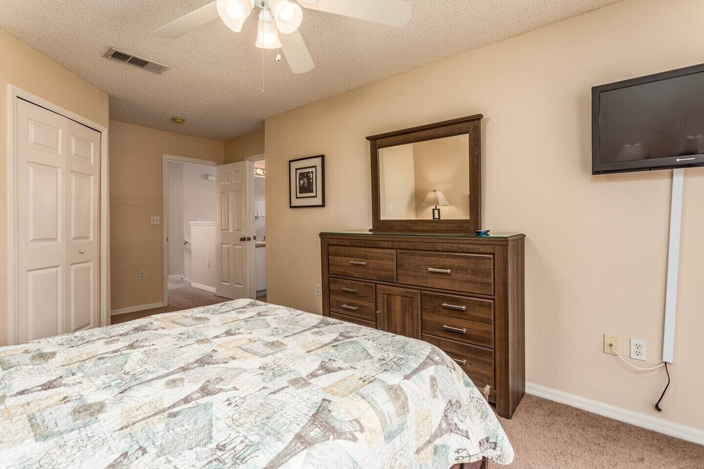 A bedroom with a bed, dresser, mirror, and television.