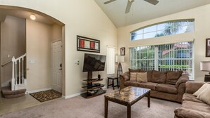 A living room with a flat-screen TV, a brown sofa, a coffee table, and a staircase leading to another room. - Last Minute Disney Getaway! Townhouse with Private Pool. Book Now! #109037 (Orlando)